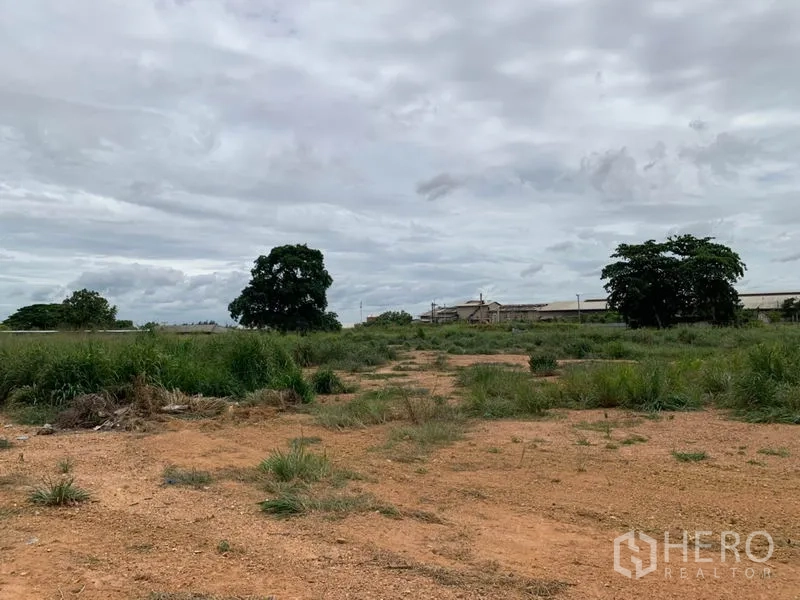 โรงงาน ให้เช่าในChon Buri - ที่ดินว่างข้างโรงงาน พื้นดินและหญ้า มีอาคารอยู่ไกลออกไป