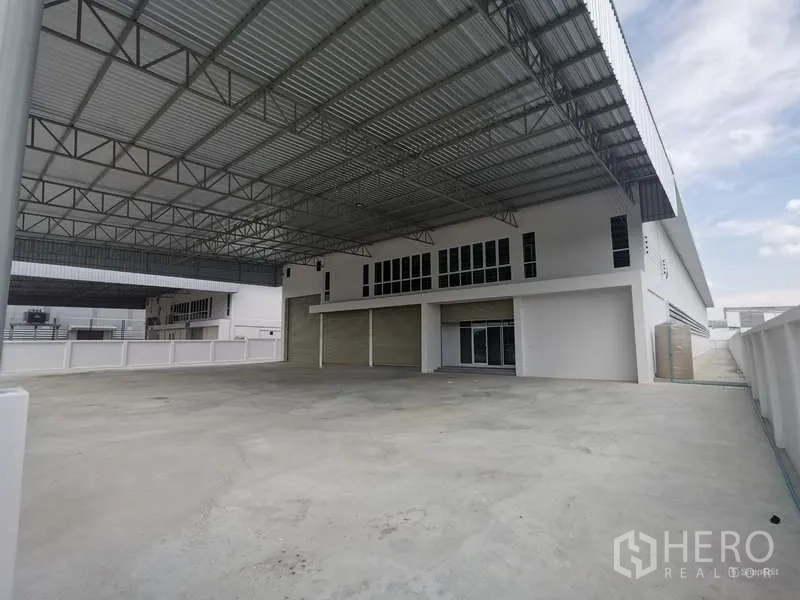 Factory for rent or sale in Bang Bo, Samut Prakan - Front perspective of the warehouse with expansive yard and high roof canopy.