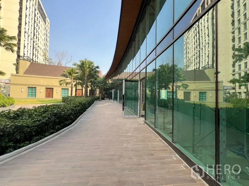 零售空间 出租在Khlong Toei, Bangkok - 沿玻璃店面的人行步道，棕榈树与铺装地面。