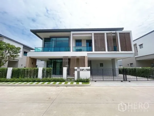 Detached House for sale in Don Mueang, Bangkok - Front view of a modern two-storey detached house with glass balcony, vertical screens, secure gate and neat landscaping.