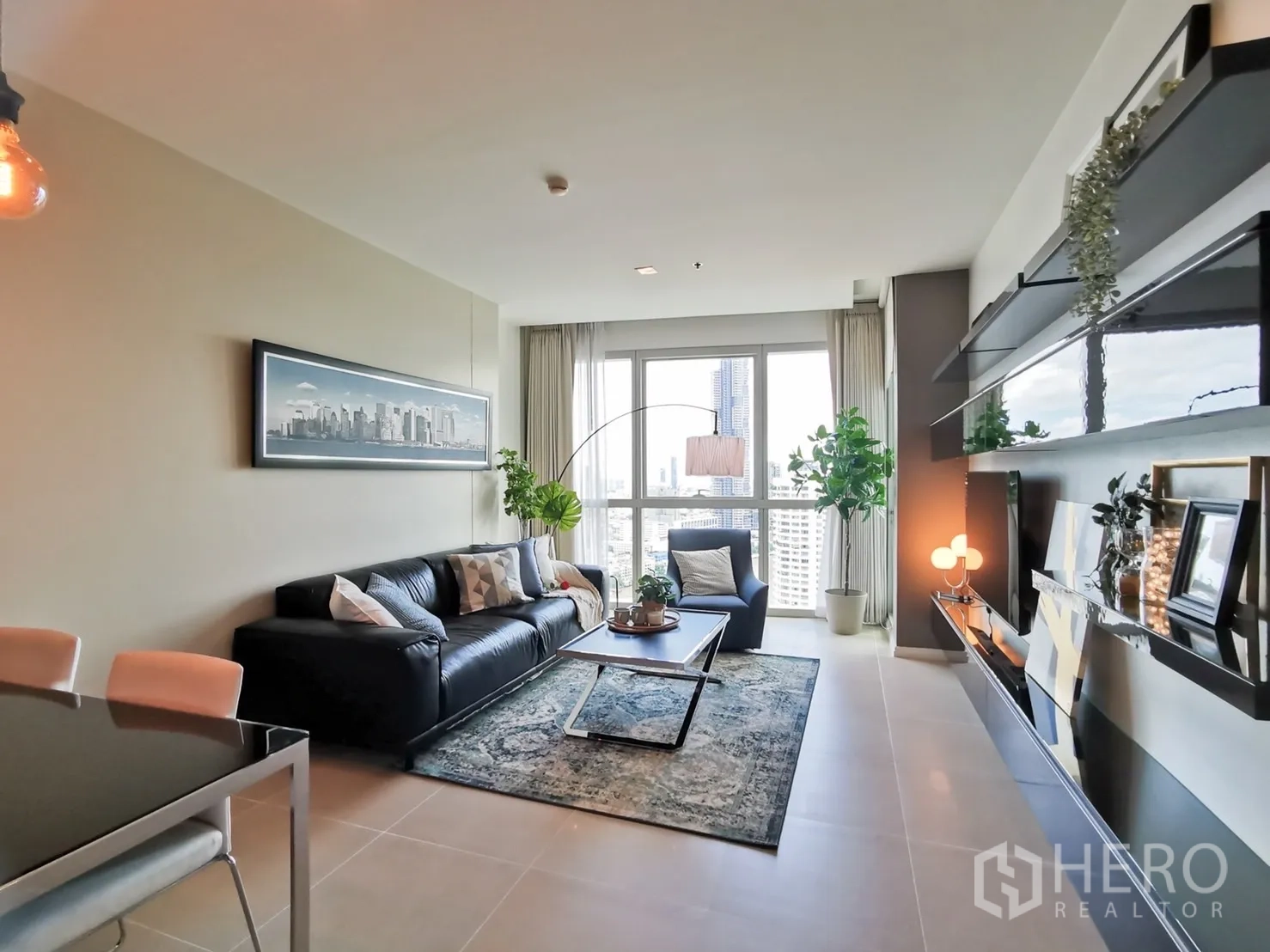 คอนโด ให้เช่าหรือขายในKhlong San, Bangkok - ห้องนั่งเล่นสว่าง โซฟาหนัง พรม ต้นไม้ และวิวเมืองผ่านหน้าต่างบานใหญ่