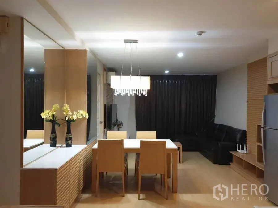 Condominium for rent in Watthana, Bangkok - Dining zone with four-seat table under crystal chandelier, mirror console, and adjoining lounge with leather sofa.