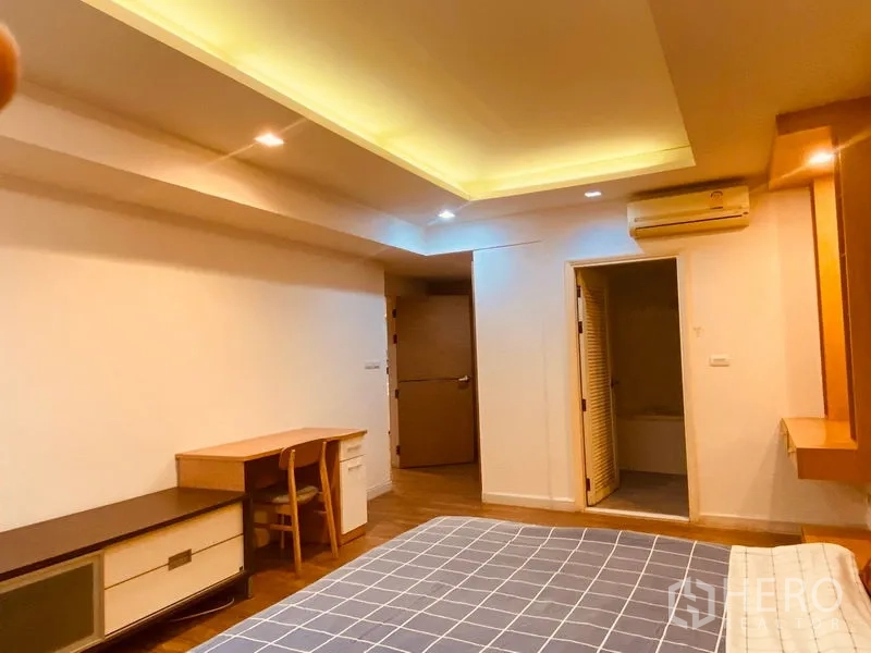Condominium for rent in Watthana, Bangkok - Bedroom with cove lighting ceiling, writing desk, wall-mounted air conditioner and an ensuite door.
