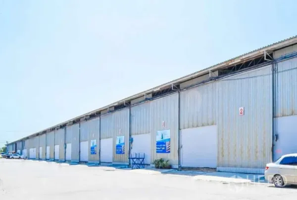 货栈 出租在Bang Sao Thong, Samut Prakan - 多联排金属外墙仓库，设多个卷帘门与停车区，天空晴朗。