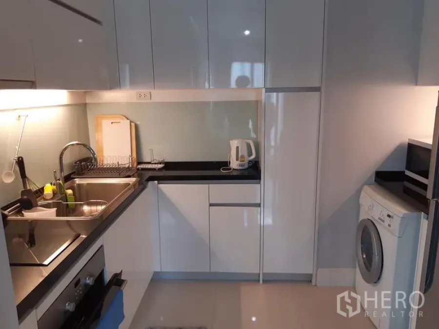 คอนโด ให้เช่าหรือขายในKhlong Toei, Bangkok - ครัวคอนโดสมัยใหม่ ตู้บานเงา เคาน์เตอร์สีดำ อ่างล้างจาน เตาอบ และเครื่องซักผ้า