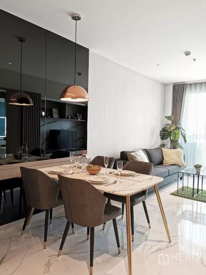 Condominium for rent in Watthana, Bangkok - Stylish dining table for four with pendant lights beside a cozy sofa and floor‑to‑ceiling windows.