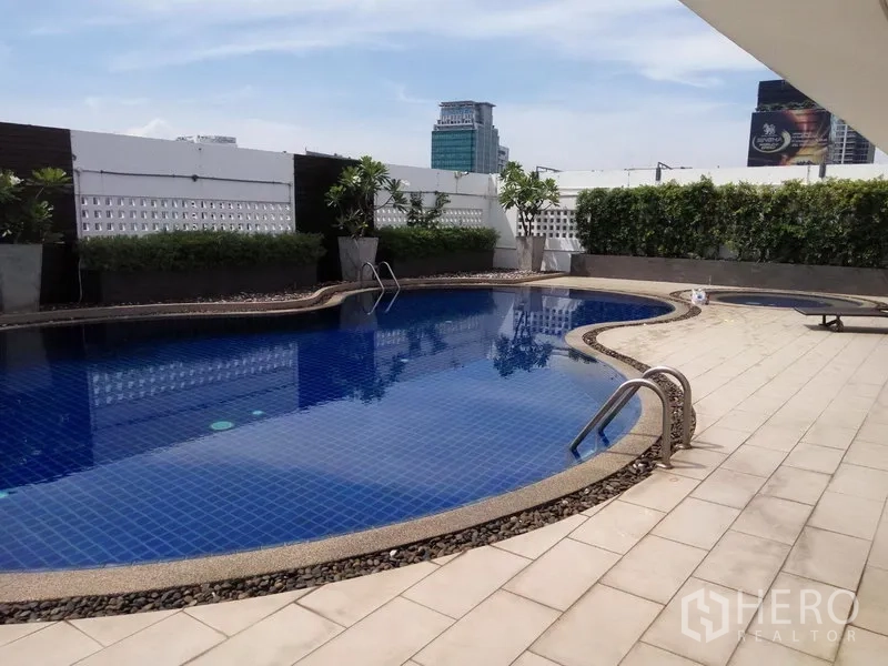 Condominium for rent or sale in Pathum Wan, Bangkok - Outdoor swimming pool with blue tiles, sun deck, and Bangkok city skyline backdrop.