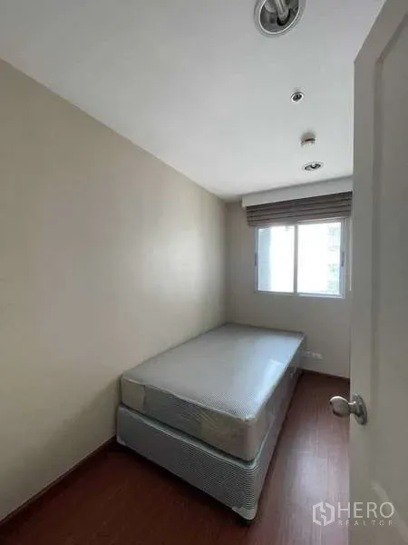Condominium for sale in Huai Khwang, Bangkok - Compact single bedroom with window, neutral walls and wood-style flooring.