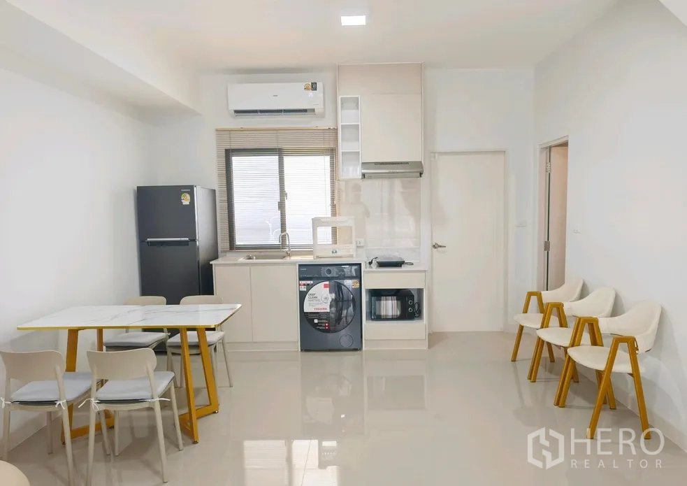 Townhouse for rent in Bang Phli, Samut Prakan - Open-plan kitchen and dining with table, refrigerator, sink, microwave, washing machine and cabinets.