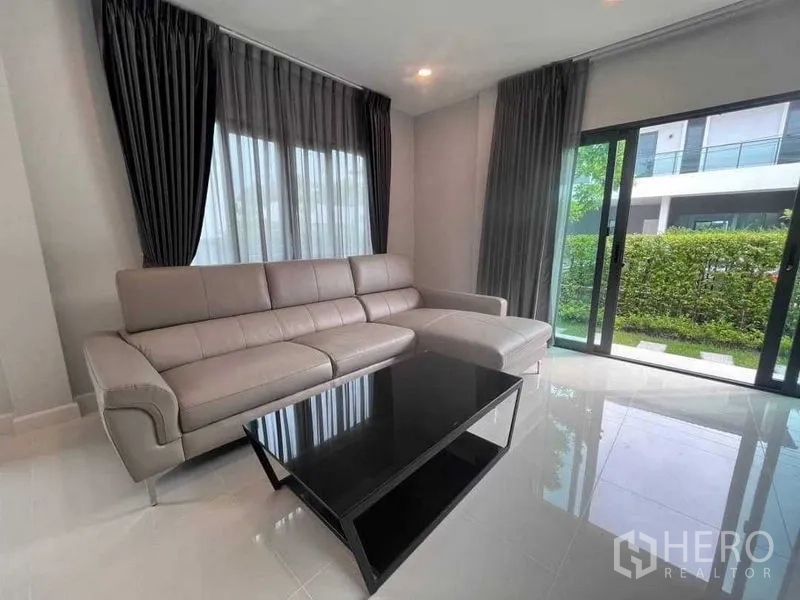 Detached House for rent in Don Mueang, Bangkok - Living room with L-shaped sofa, black coffee table and floor-to-ceiling glass.