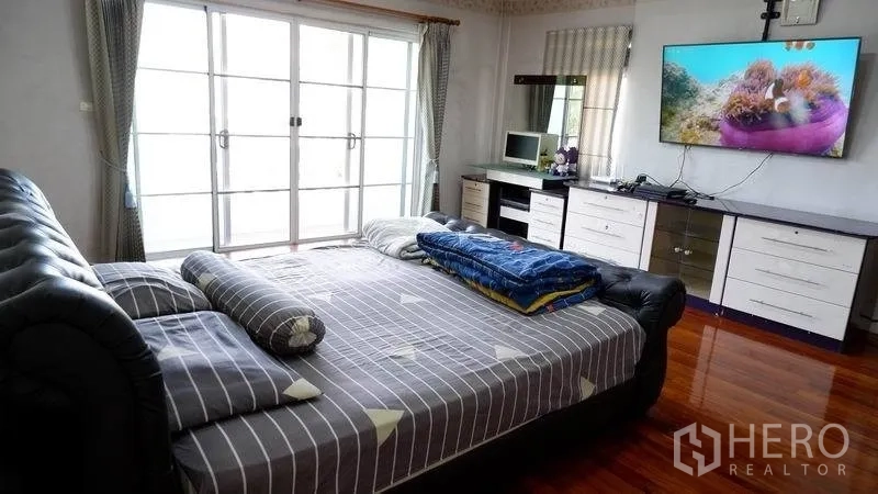 Detached House for rent in Prawet, Bangkok - Spacious master bedroom with large bed, wall-mounted TV and sliding glass doors to a balcony.