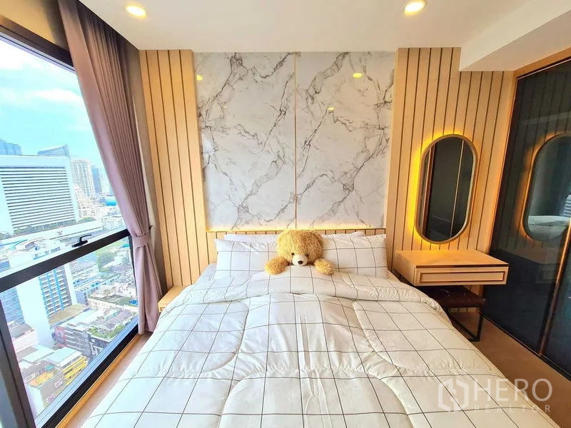Condominium for rent in Bang Rak, Bangkok - Bedroom with marble accent wall, bedside vanity and a large window with city view.