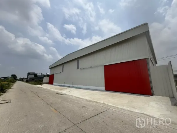 คลังสินค้า ให้เช่าในLam Luk Ka, Pathum Thani - มุมด้านข้างตัวอาคาร โชว์แนวอาคารยาว ประตูแดง และพื้นที่คอนกรีตกว้างสำหรับรถบรรทุก