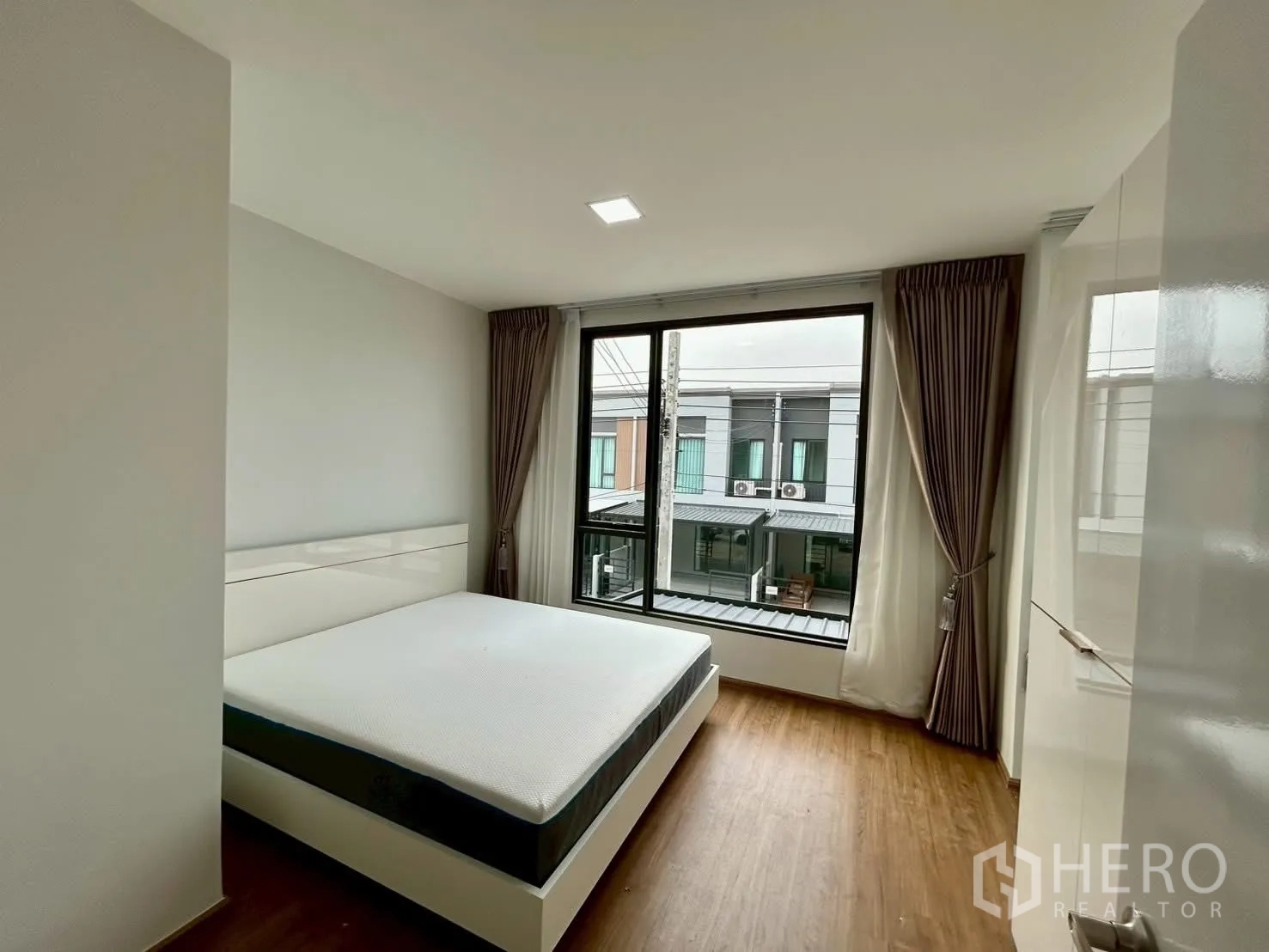 Townhouse for rent in Bang Phli, Samut Prakan - Bedroom with large window overlooking neighboring townhouses.