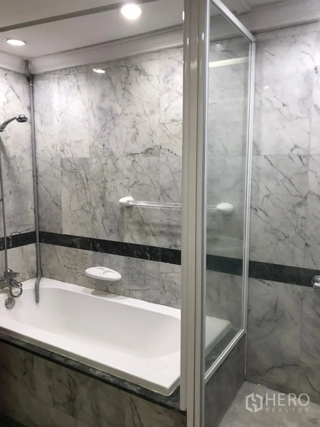 Condominium for rent or sale in Pathum Wan, Bangkok - Marble bathroom with bathtub, handheld shower and glass shower partition under recessed lighting.