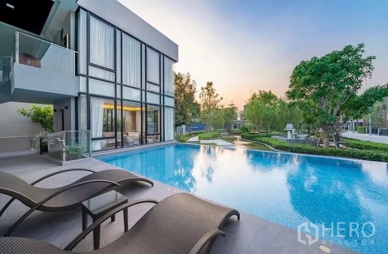 Townhouse for rent or sale in Saphan Sung, Bangkok - Community swimming pool beside a modern glass-walled clubhouse with sun loungers.
