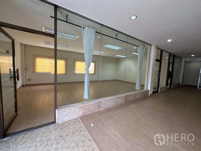 Warehouse for rent in Suan Luang, Bangkok - Glass-walled studio-style room with curtains and recessed lighting along a corridor.