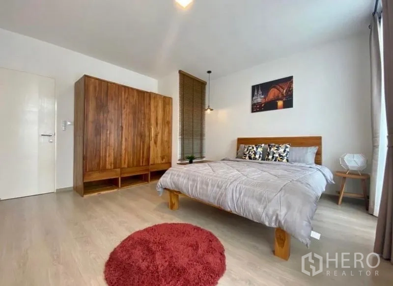 ทาวน์เฮาส์ ให้เช่าในBang Phli, Samut Prakan - ห้องนอนใหญ่ ตู้เสื้อผ้าไม้ โต๊ะข้างเตียง และพรมกลมบนพื้นไม้สีอ่อน