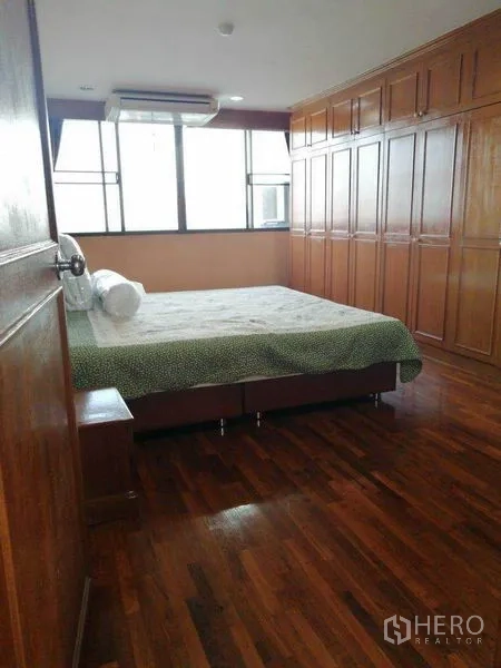 Condominium for rent in Watthana, Bangkok - Bedroom with wall-to-wall wooden wardrobes, bed and large window.