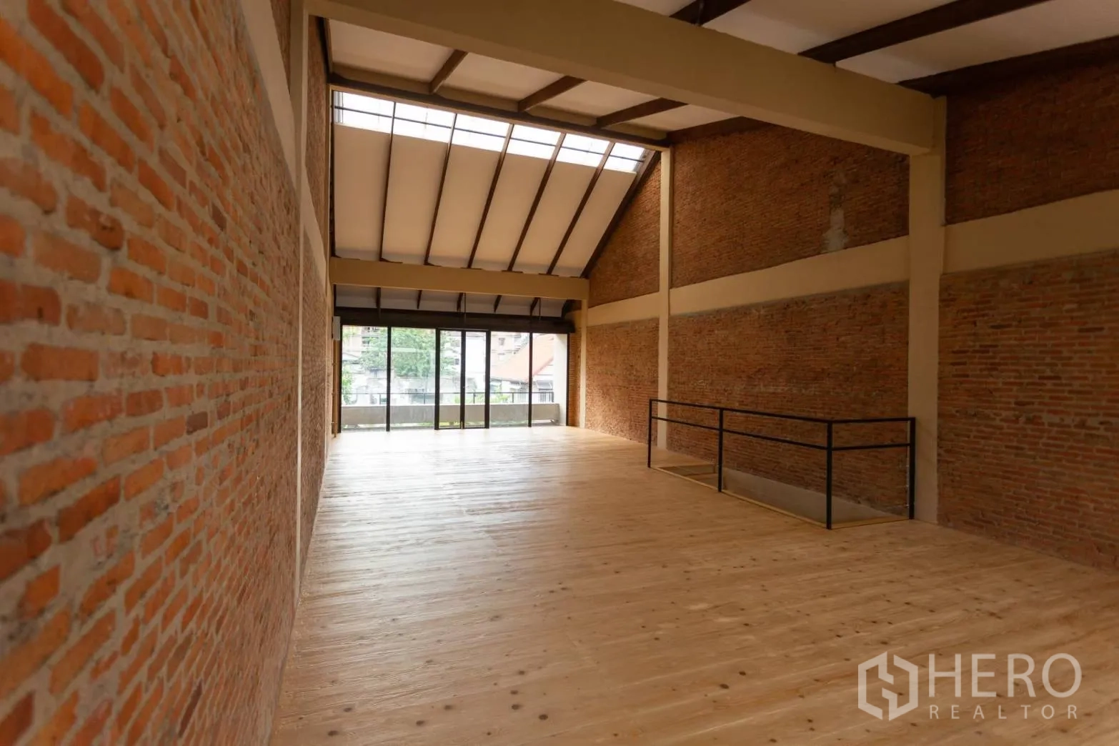 Home Office for rent in Watthana, Bangkok - Open column‑free upper floor with high ceiling, skylight, brick feature walls and wood flooring.