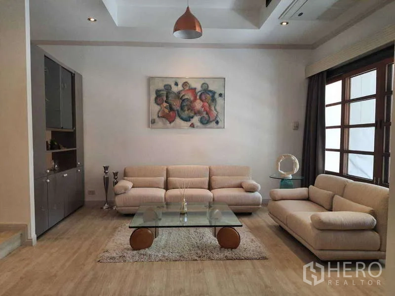 ทาวน์เฮาส์ ให้เช่าในKhlong Toei, Bangkok - มุมนั่งเล่นโทนอบอุ่น โซฟาสีเบจและโต๊ะกระจกพร้อมภาพศิลป์