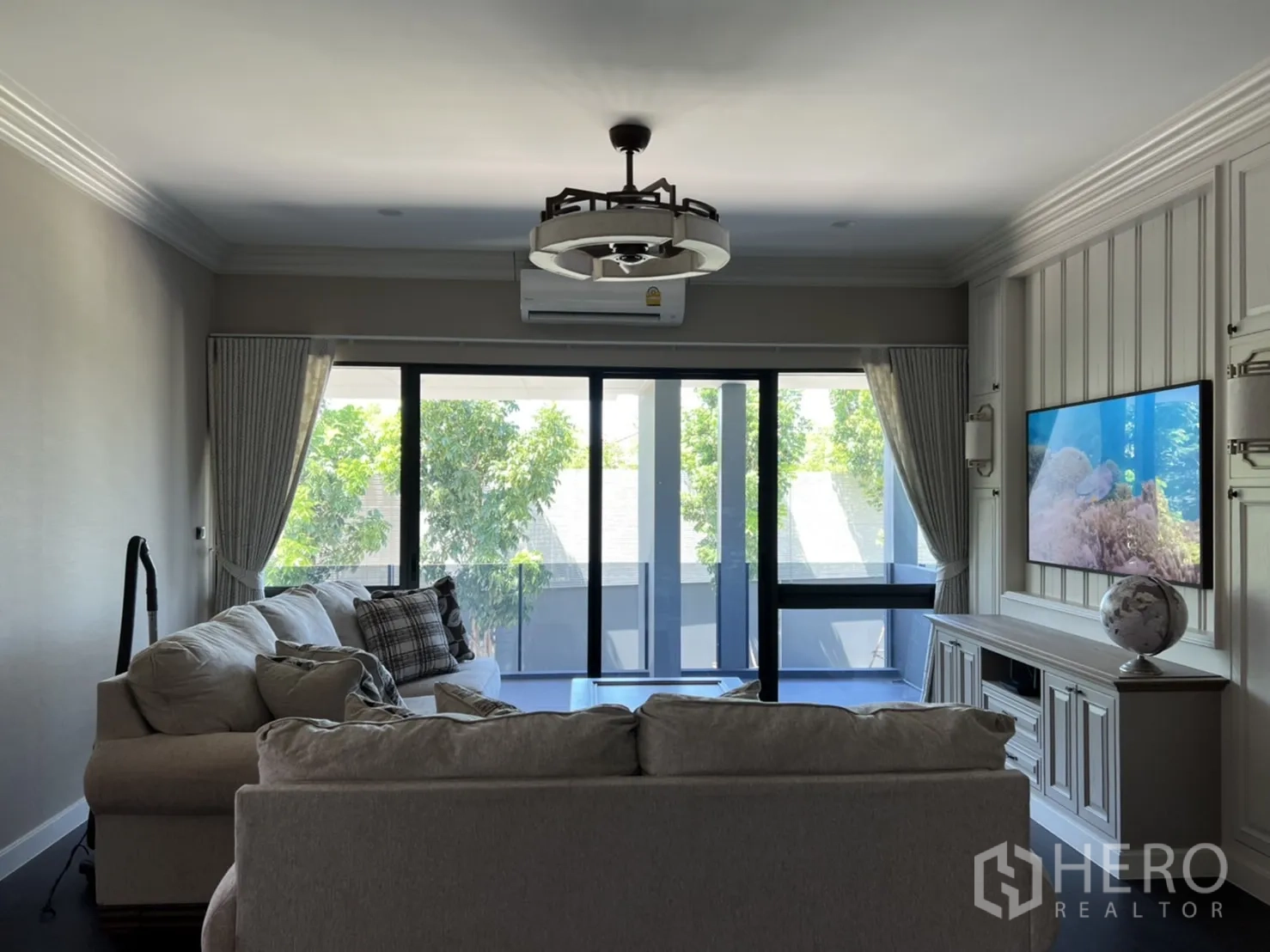 Detached House for rent or sale in Bang Kapi, Bangkok - Upstairs family room with sofas, wall-mounted TV and wide sliding doors opening to a balcony with green views.