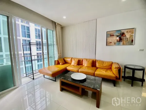 คอนโด ให้เช่าในWatthana, Bangkok - ห้องนั่งเล่นสว่าง โซฟาหนังสีส้ม โต๊ะกลางหินอ่อน ประตูบานเลื่อนออกระเบียง มองเห็นอาคารใกล้เคียง