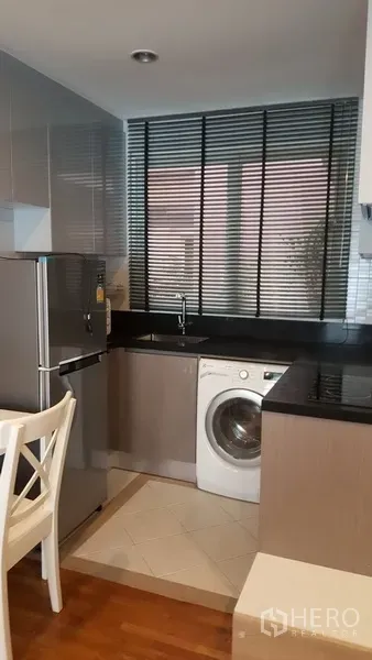 Condominium for rent in Watthana, Bangkok - Compact kitchen with black countertops, window blinds, stainless refrigerator, and a front-load washing machine.