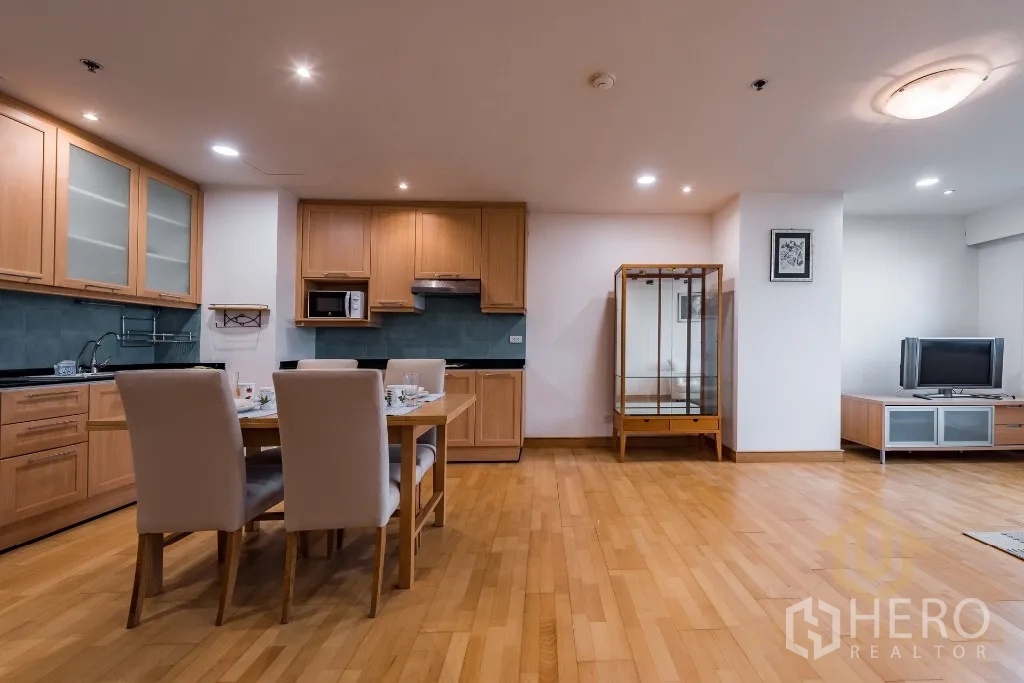 Condominium for rent or sale in Pathum Wan, Bangkok - Spacious living–dining room with fitted kitchen, display cabinet, and TV console on hardwood floors.