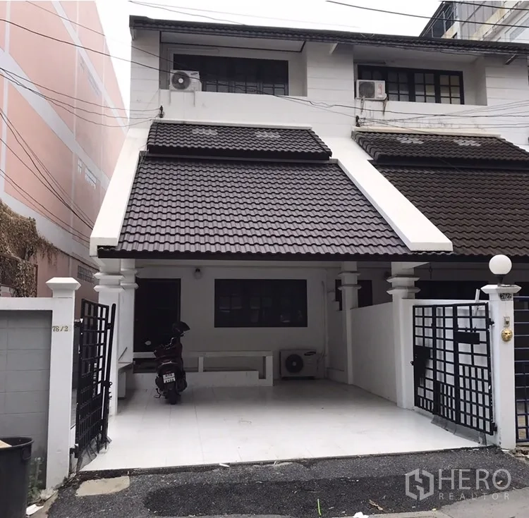 联排别墅 出租在Watthana, Bangkok - 白色两层联排别墅外观，深色瓦屋顶，带大门和有顶车位