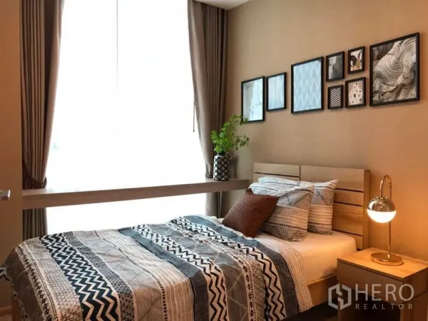 คอนโด ขาย - ห้องนอนที่สองอบอุ่น กรอบรูปติดผนัง ผ้าปูเตียงลายกราฟิก โต๊ะยาวใต้มุมหน้าต่าง และโคมไฟหัวเตียง