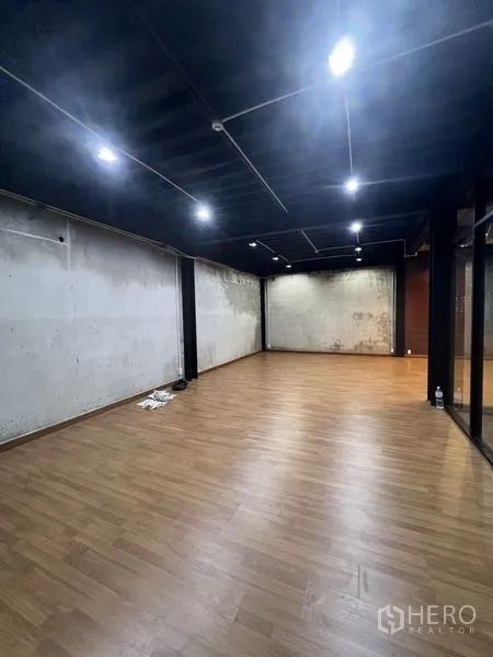 办公空间 出租在Khlong Toei, Bangkok - 开放式办公室内景，木纹地板、黑色裸露天花与LED射灯、水泥墙面。