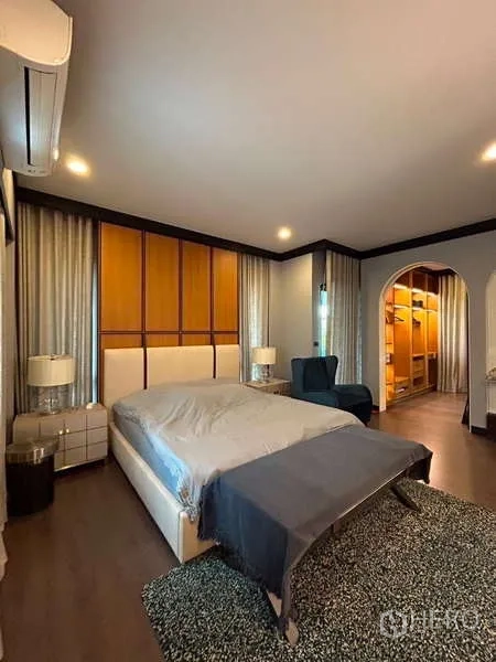 Detached House for rent in Bang Kapi, Bangkok - Master bedroom with upholstered bed, rug, and arched entry leading to an illuminated walk-in closet.