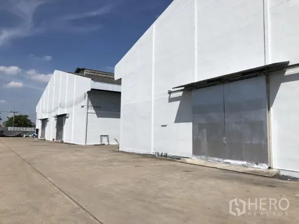 货栈 出租在Mueang Pathum Thani, Pathum Thani - 白色仓库外立面，宽阔混凝土场地与大型钢制推拉门，位于封闭园区。