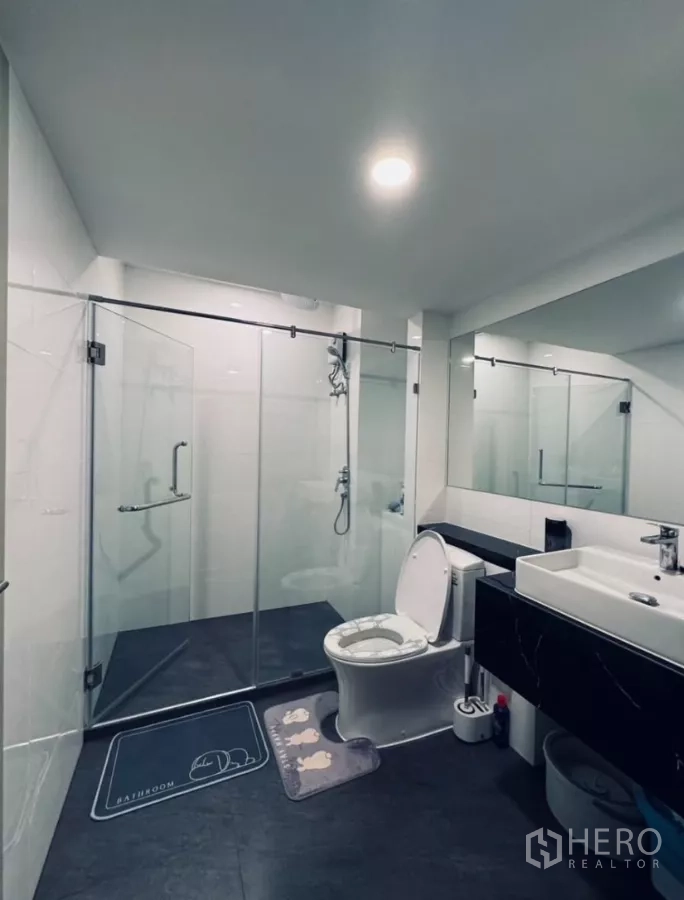 Condominium for rent in Chatuchak, Bangkok - Spacious bathroom with glass shower, vanity, and toilet.