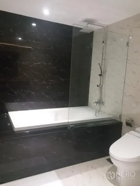 Condominium for rent in Bang Rak, Bangkok - Modern bathroom featuring a bathtub with glass screen, black marble wall and white tiles.