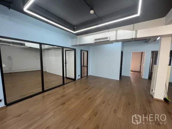 Office Space for rent in Khlong Toei, Bangkok - Corner view of office showing glass conference room doors, exposed ceiling with ducts and wood laminate flooring.