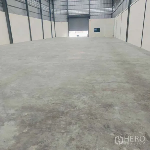 货栈 出租在Ban Phaeo, Samut Sakhon - 仓库内部空间宽敞，混凝土地面，高挑钢结构天花，尽头为卷闸门。
