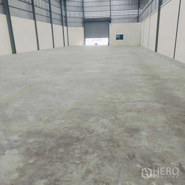 货栈 出租在Ban Phaeo, Samut Sakhon - 仓库内部空间宽敞，混凝土地面，高挑钢结构天花，尽头为卷闸门。