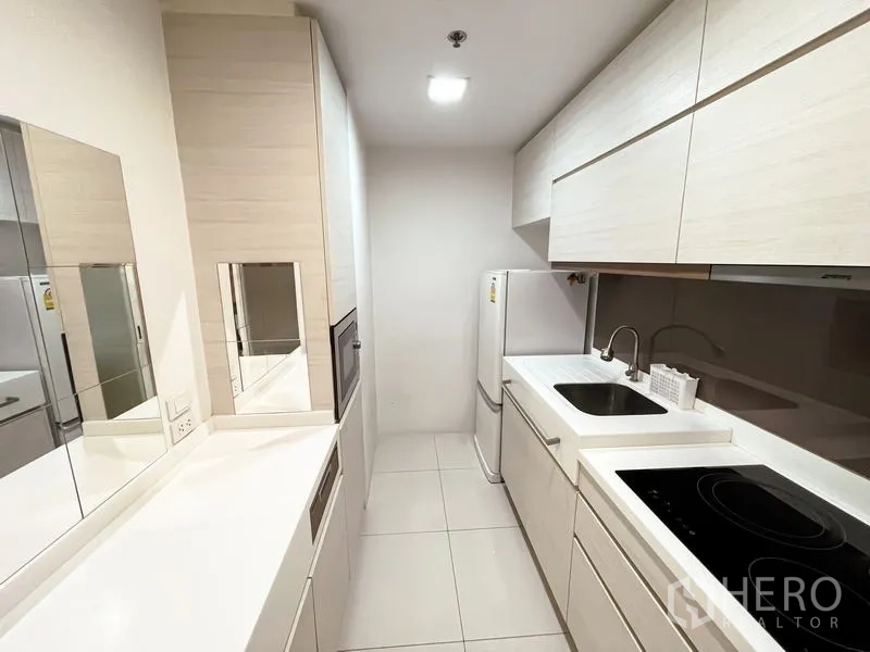 คอนโด ขาย - ครัวแบบแกลเลย์ตู้สีขาว ซิงก์ เตาไฟฟ้า และตู้เย็น