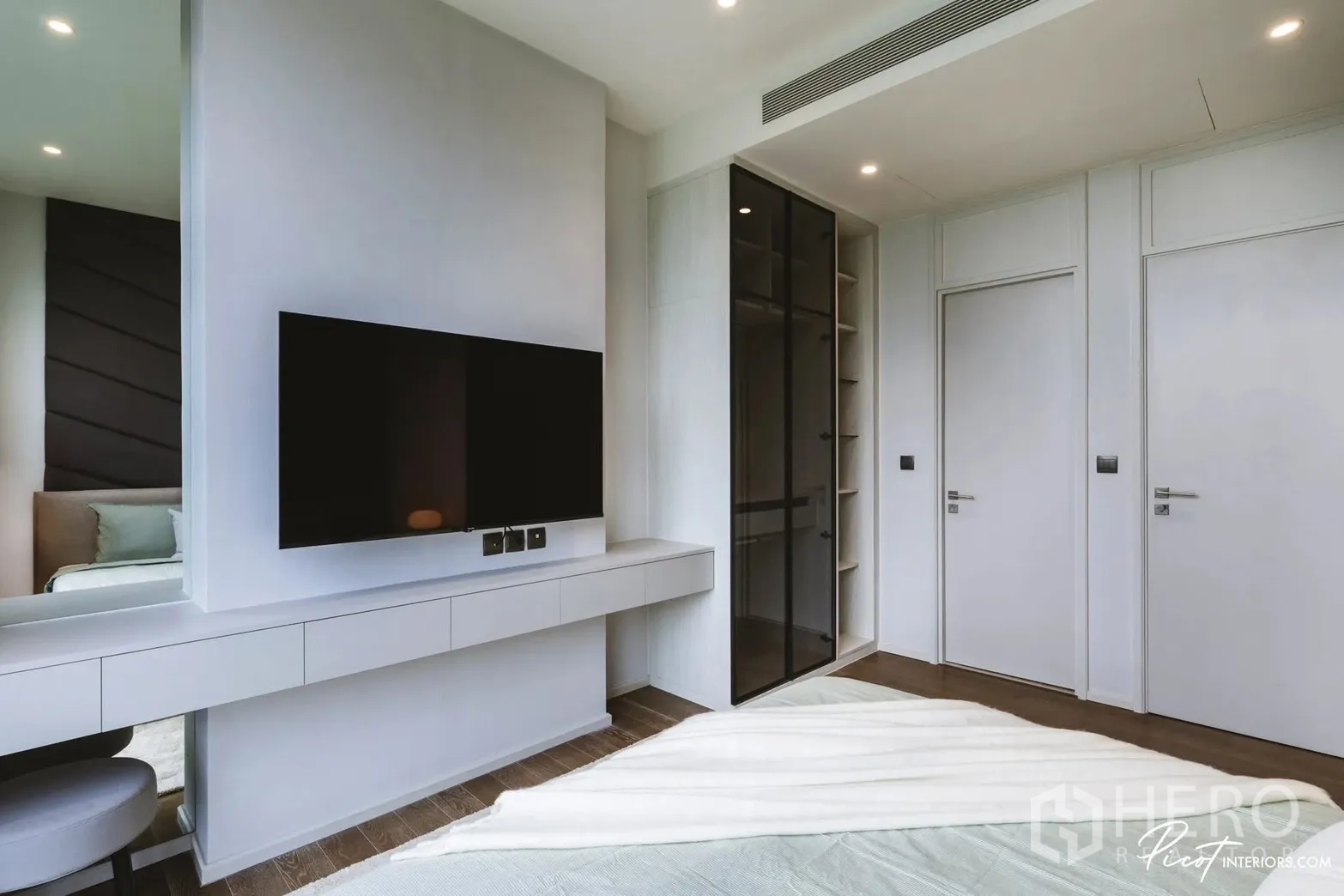 Condominium for rent in Pathum Wan, Bangkok - Bedroom with wall-mounted TV and built-in wardrobe behind tinted glass doors.