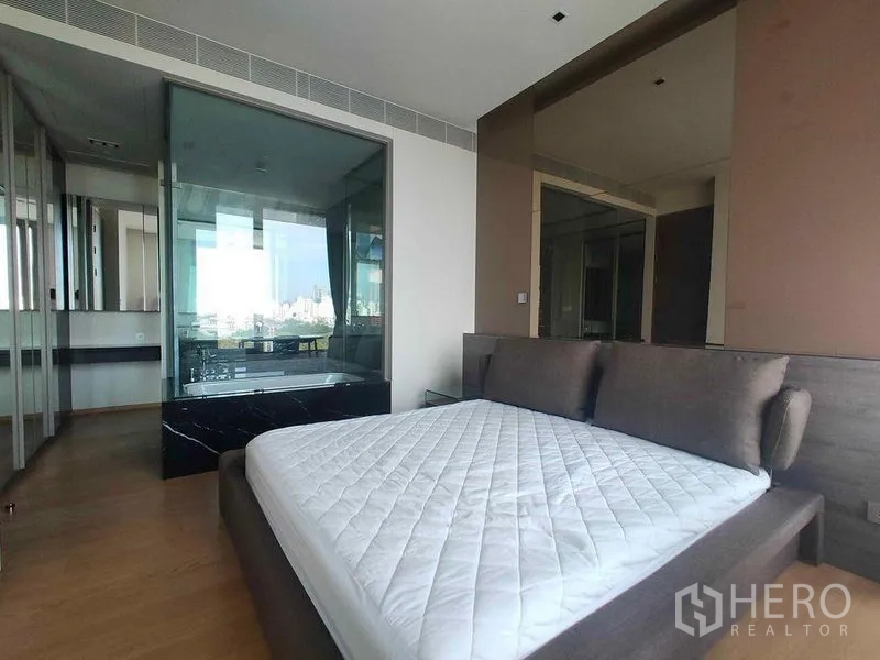 公寓 出租在Bang Rak, Bangkok - 卧室配软包床，浴室玻璃隔断与衣柜，可欣赏城市天际线。