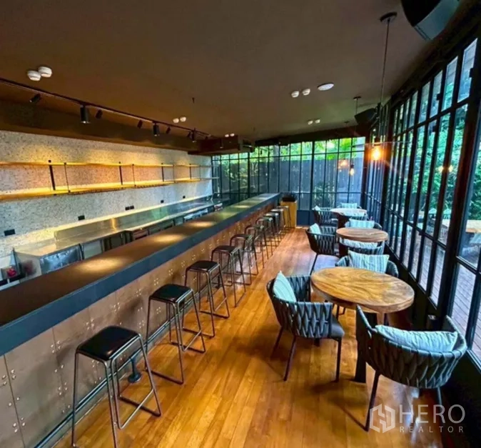 零售空间 出租在Yan Nawa, Bangkok - 长吧台配高脚凳，圆桌用餐区，落地窗面向花园庭院。