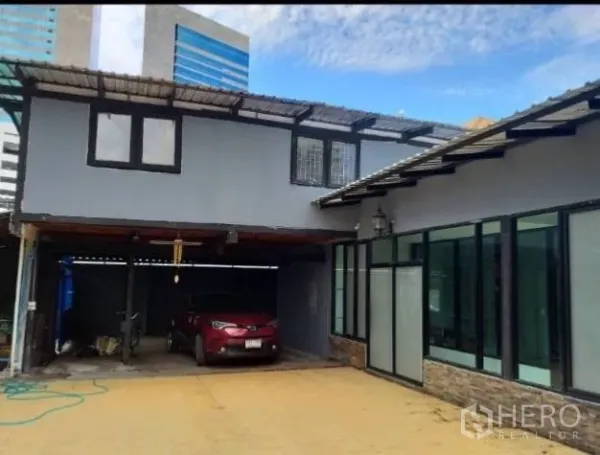 Detached House for rent in Khlong Toei, Bangkok - Two-storey house exterior with carport and city buildings in the background