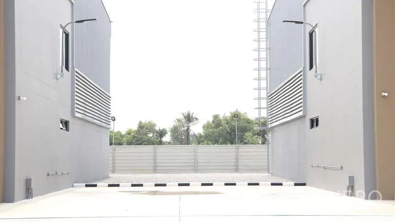 Warehouse for rent in Sam Phran, Nakhon Pathom - Rear service lane between buildings with a secure fence and street lighting.