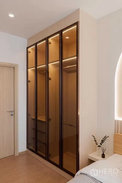 Condominium for rent in Watthana, Bangkok - Tall glass-door wardrobe with interior lighting beside a bedroom door.