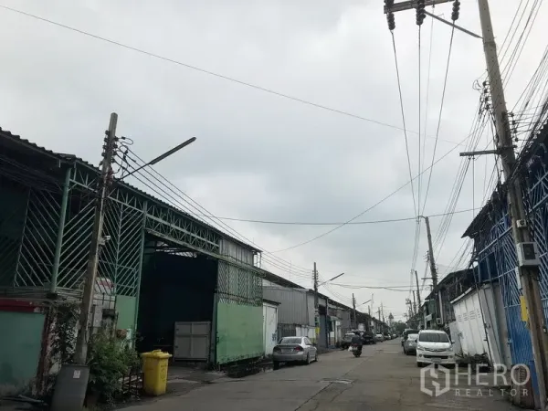 Warehouse for rent in Bang Phli, Samut Prakan - Industrial lane outside a row of metal warehouses with road access and overhead power lines in Bang Phli.