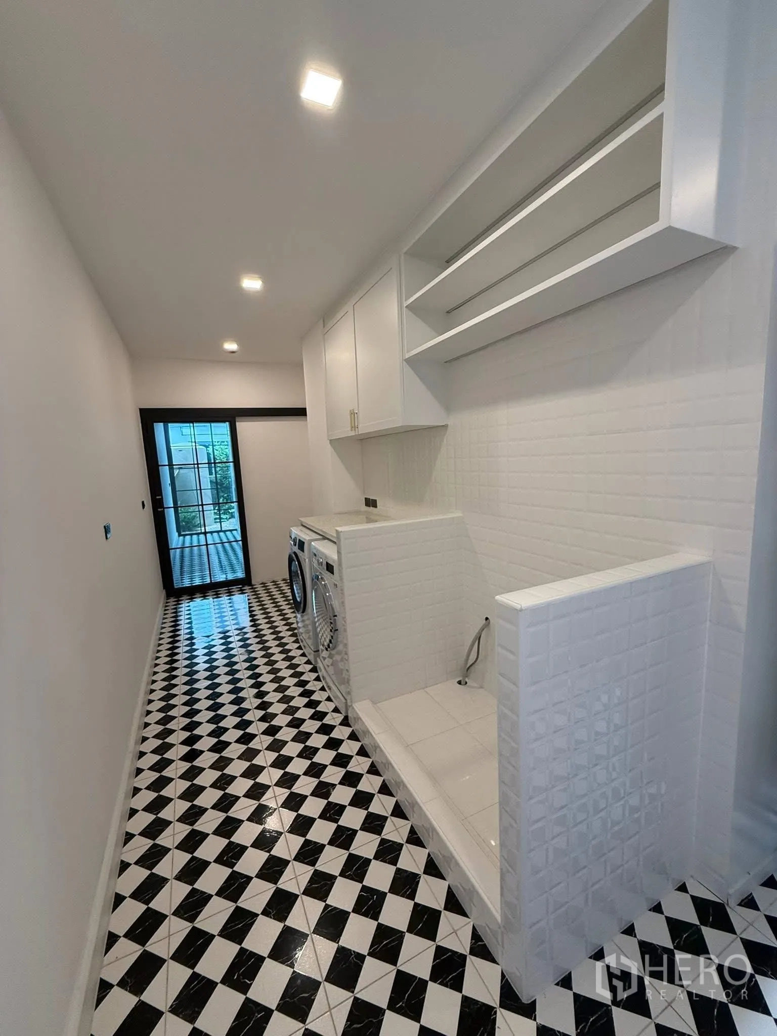 บ้าน ขายในBang Kruai, Nonthaburi - ห้องซักรีดมีเครื่องซักผ้า‑อบผ้า อ่างอเนกประสงค์ และพื้นลายตารางต่อเนื่องสู่ประตูหลังบ้าน