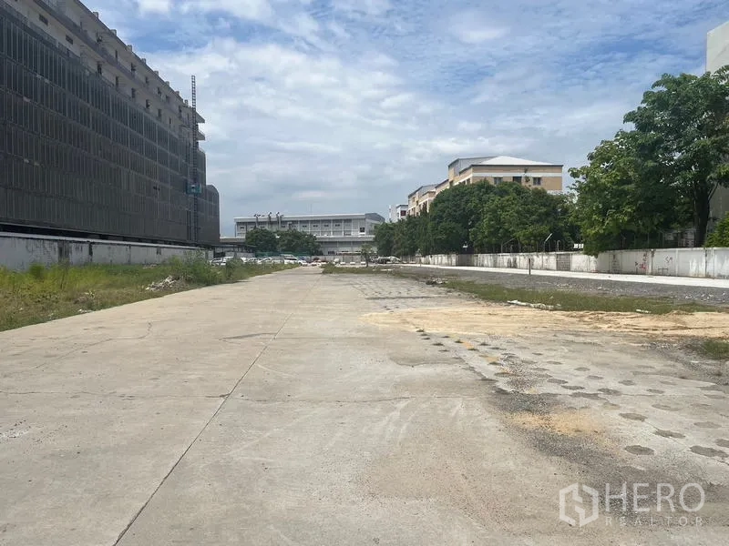 ที่ดิน ให้เช่าในBang Khun Thian, Bangkok - พื้นที่โล่งกว้างพื้นคอนกรีต มีรั้วกำแพงล้อม ระหว่างอาคารเตี้ยและแนวต้นไม้