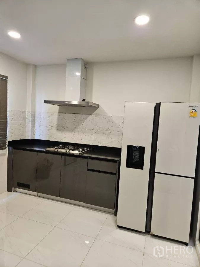 Detached House for rent or sale in Bang Phli, Samut Prakan - Cooking zone with gas hob, chimney hood, and double‑door refrigerator in the Thai kitchen.